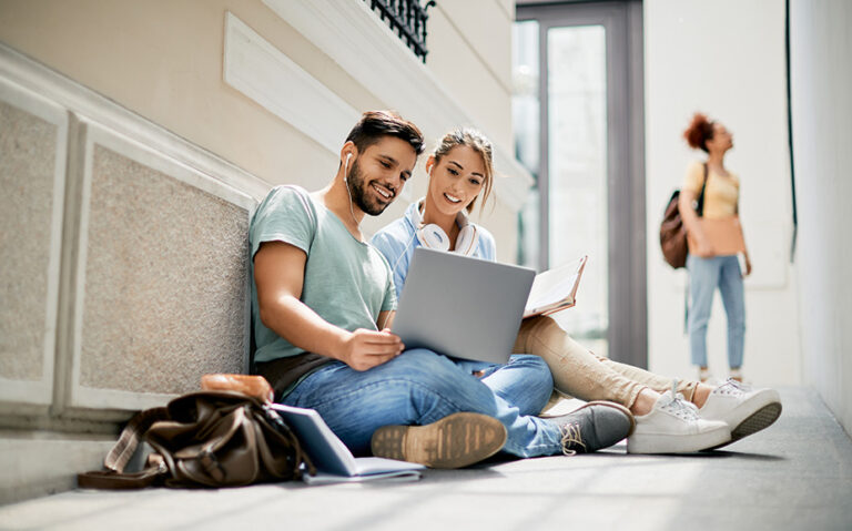Two young adults sit together and look at a laptop with a smile.