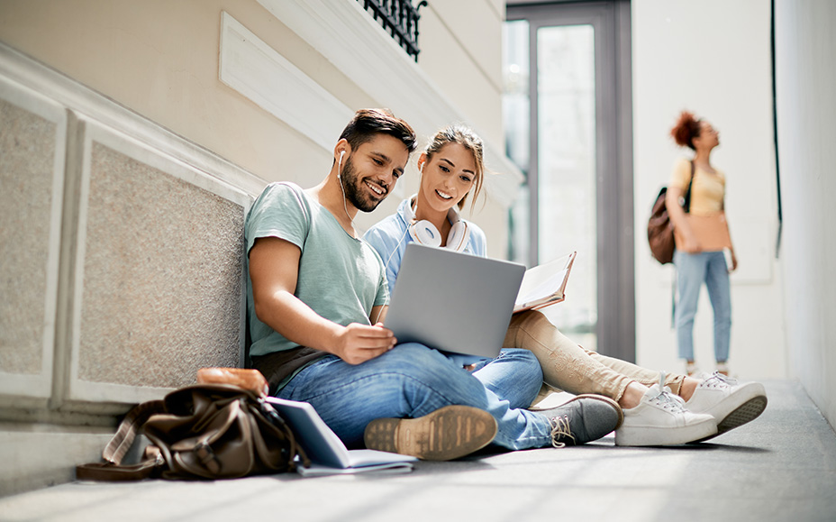 Two young adults sit together and look at a laptop with a smile.