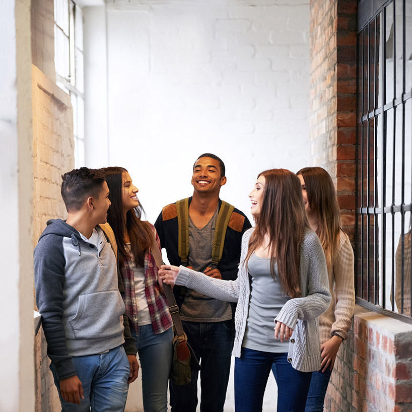 Five young adults walk down a hallway and talk laughing.