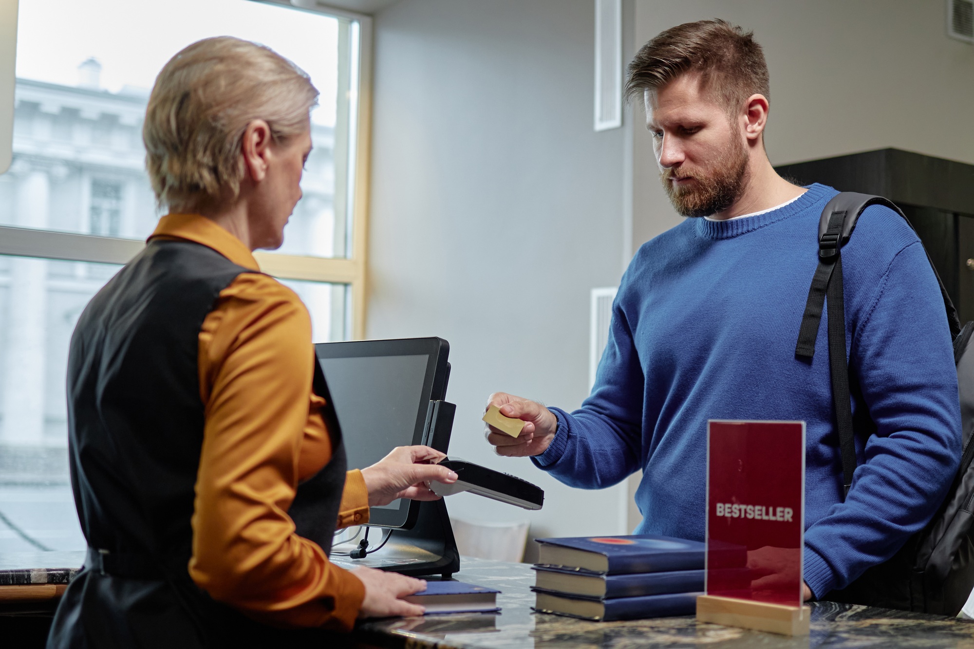 Caucasian Young Adult Man Paying Librarian for Books at Checkout Counter