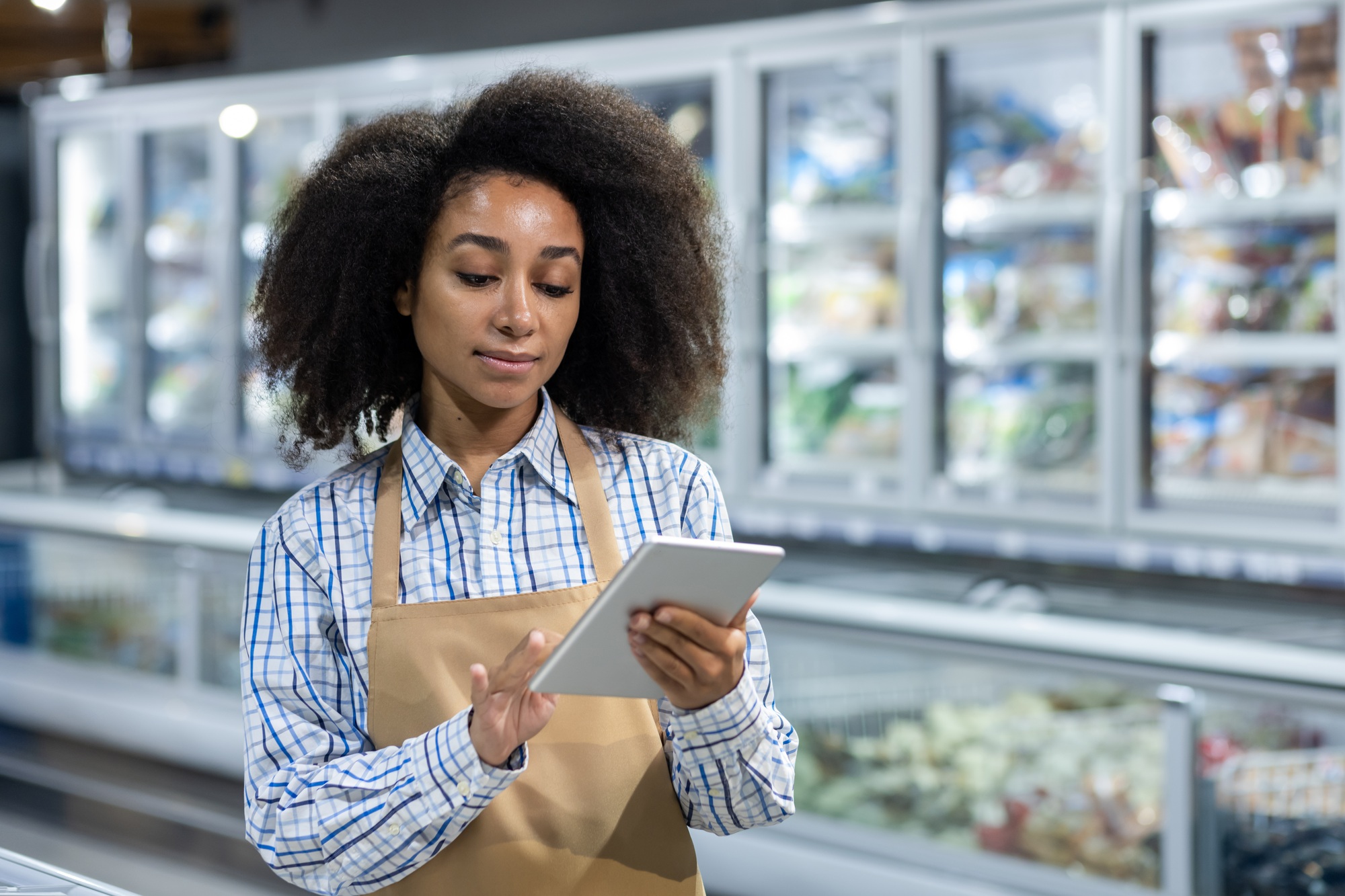 Female supermarket employee using digital tablet in frozen foods section