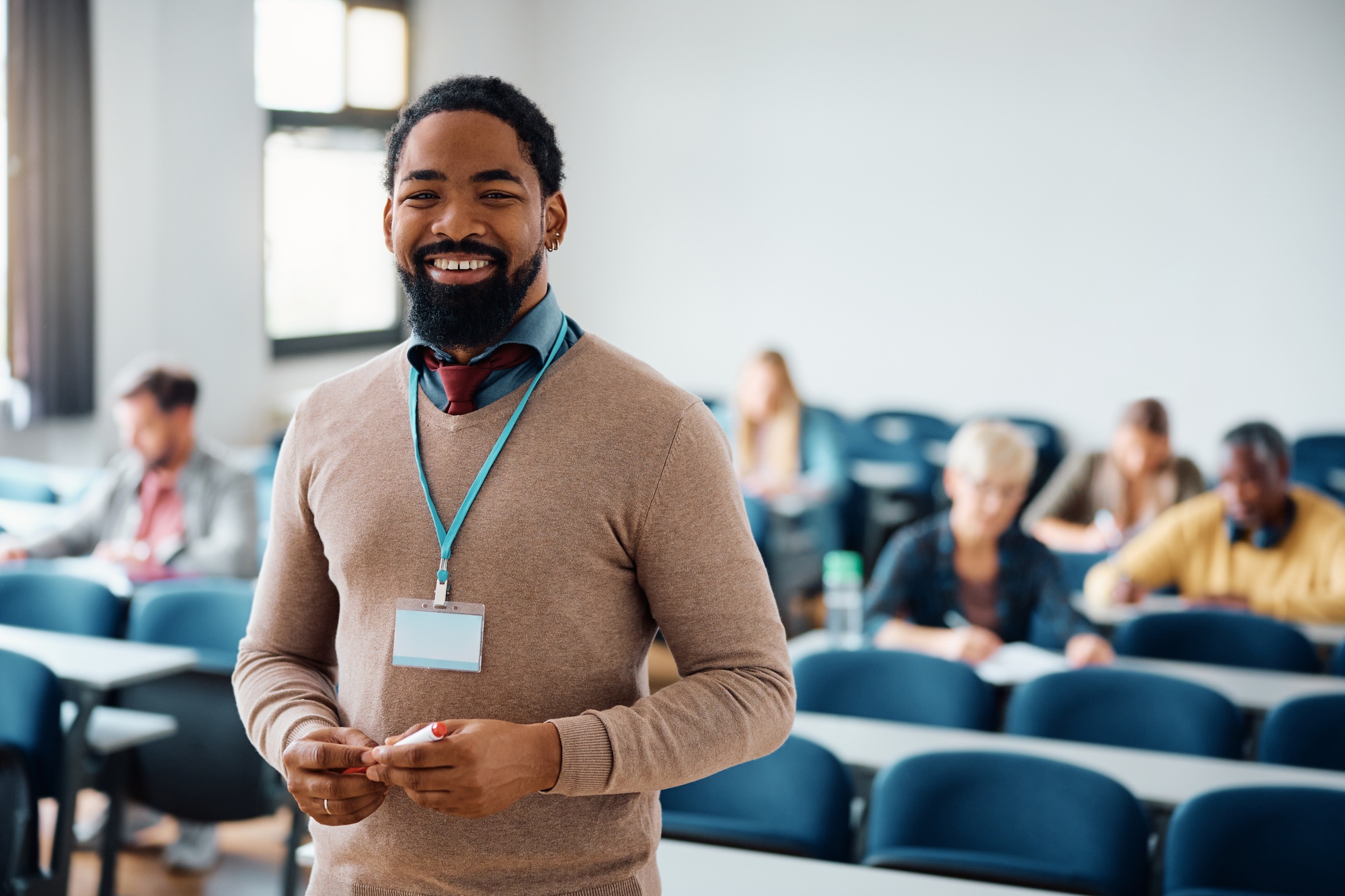 Happy black adult education teacher in lecture hall looking at camera.